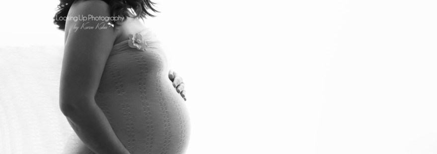 Black and white back-lit expecting mommy draped in lovely lace fabric cradling belly for posed maternity portrait session