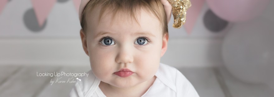 Pouty cuteness in gold and pink themes themed cake smash session for one year old milestone baby girl looking adorable in onesie with gray polka dots for 12 month portrait