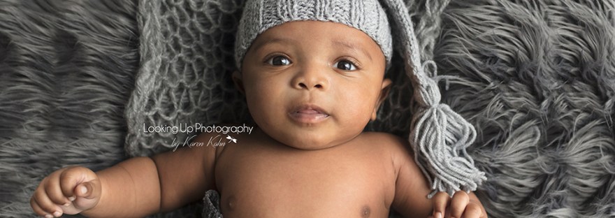 Aerial view of precious baby boy laying on gray furry rug with a gray knit hat for 3 month milestone portrait session