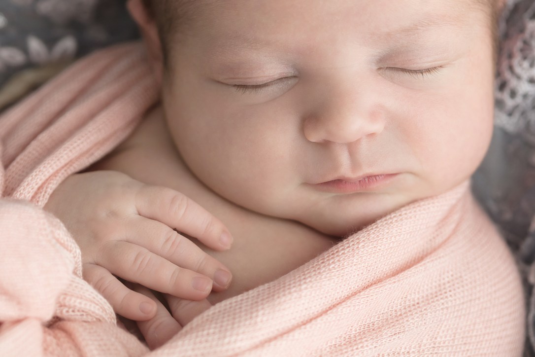 Close-up of eye lashes and hands for newborn portrait session of baby girl swaddled in peach wrap surrounded by gray lace