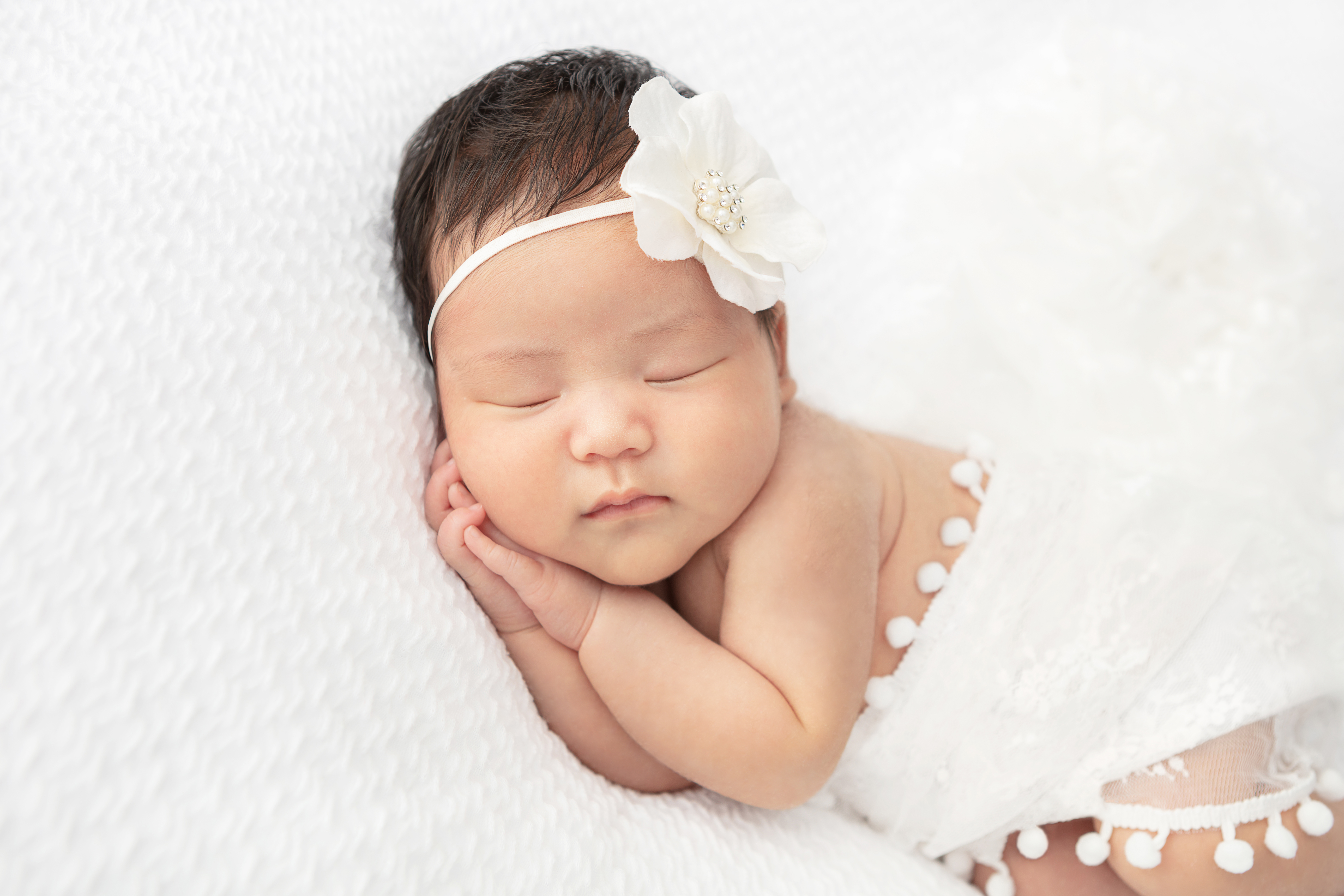 baby newborn girl with lots of dark hair wearing a large floral white headband