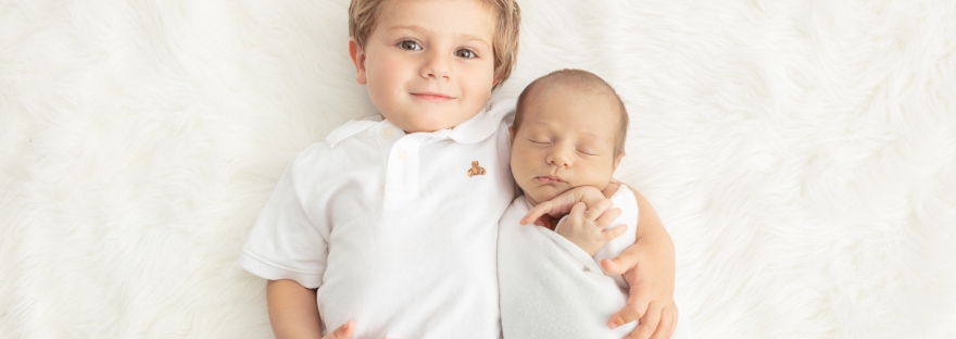 proud toddler brother with his arm around his new baby brother