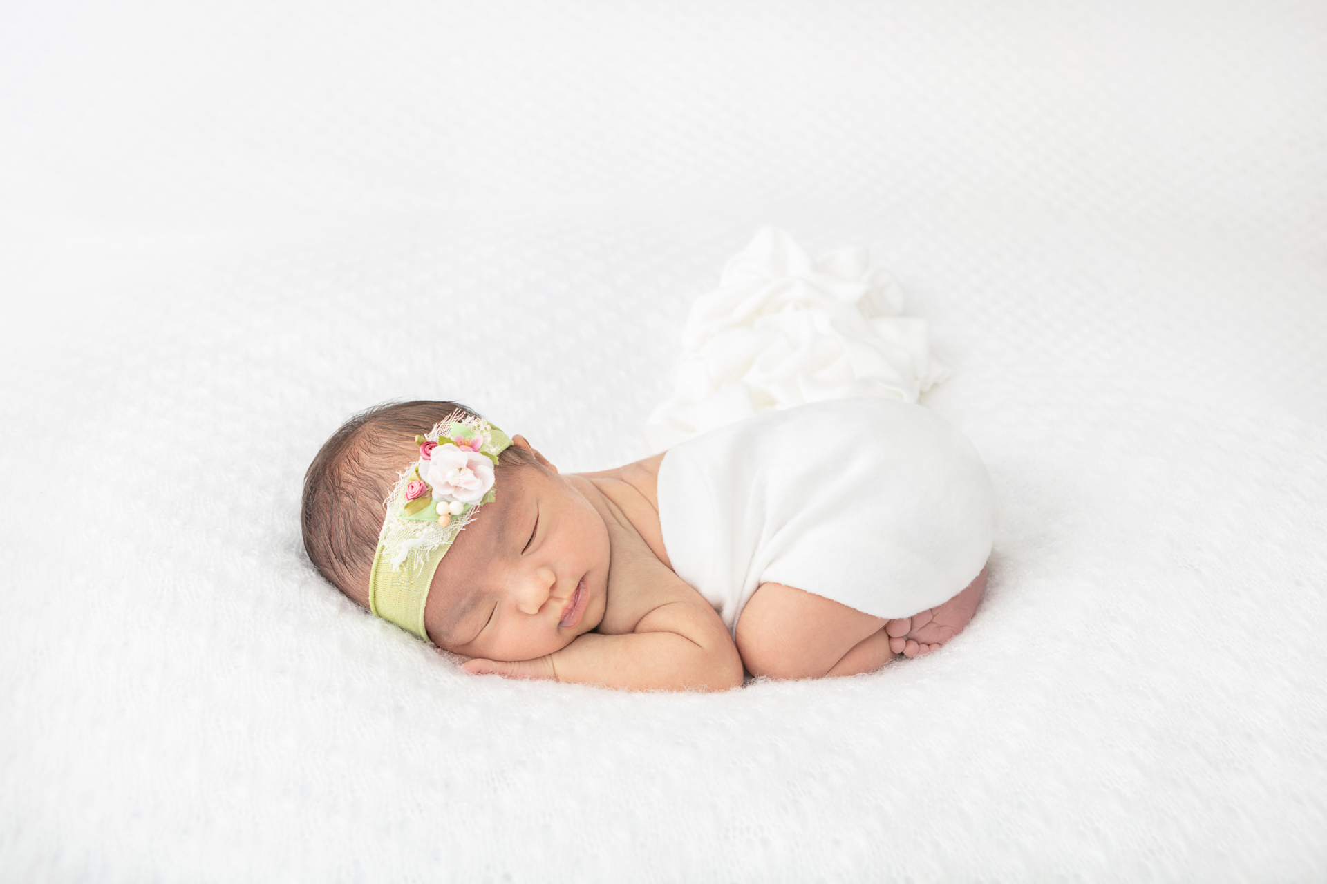 newborn baby girl with dark hair wearing a lime green stretchy headband with white and pink florals