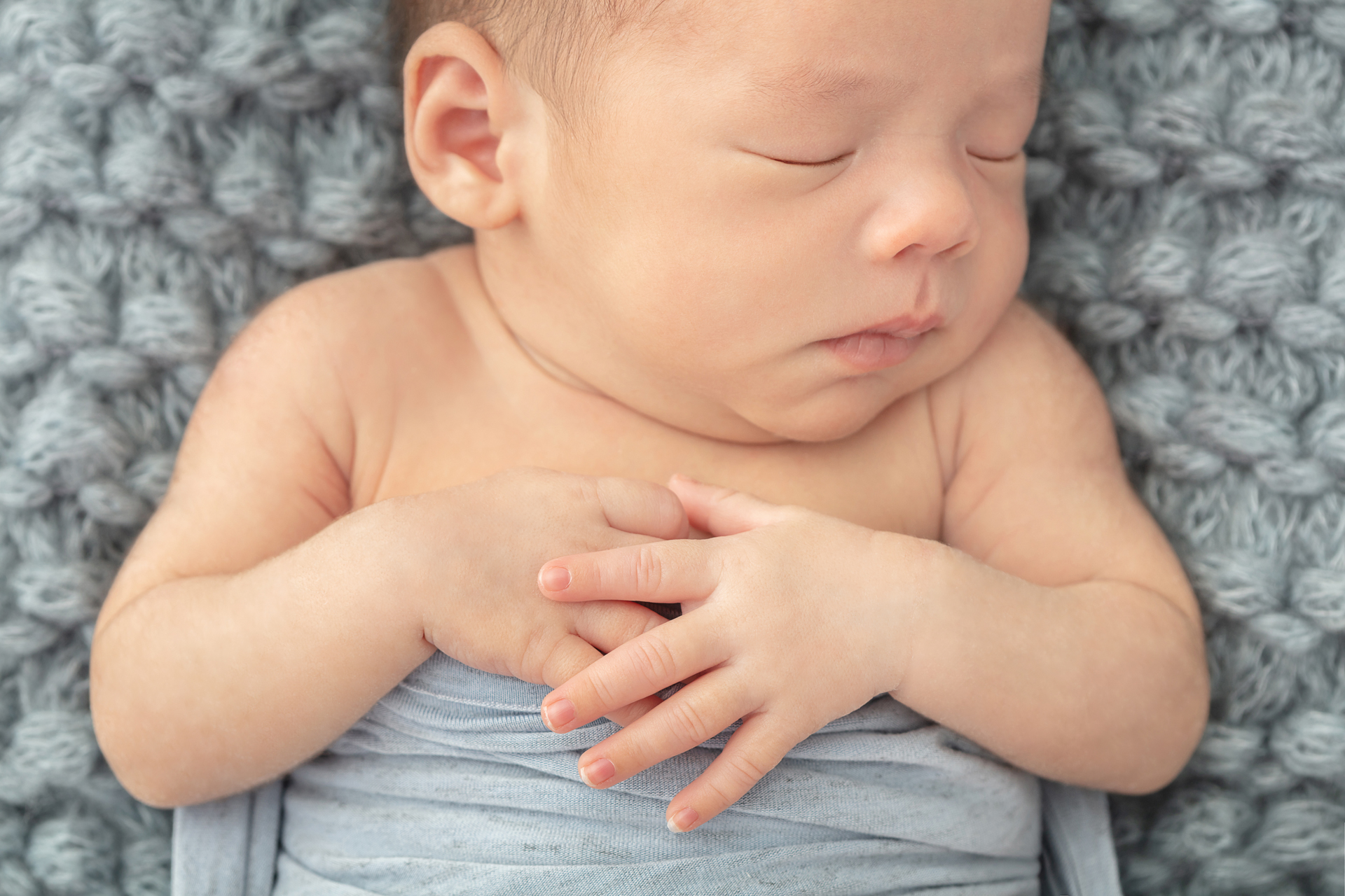 sweet newborn baby boy with his hands folded across his chest; chunky knit dusty blue blanket