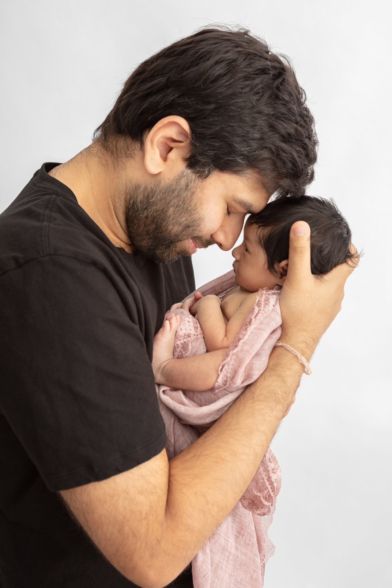 new father leaning his head down to touch foreheads with his newborn baby girl who has her eyes open