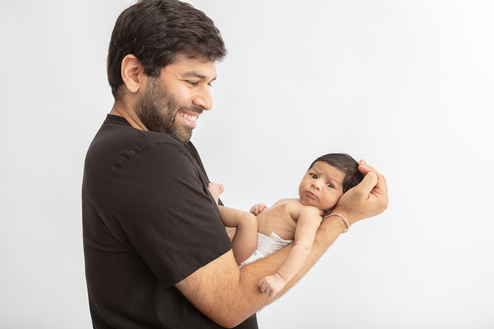 smiling new father grinning at his newborn baby daughter who is looking at the camera and making a funny newborn face