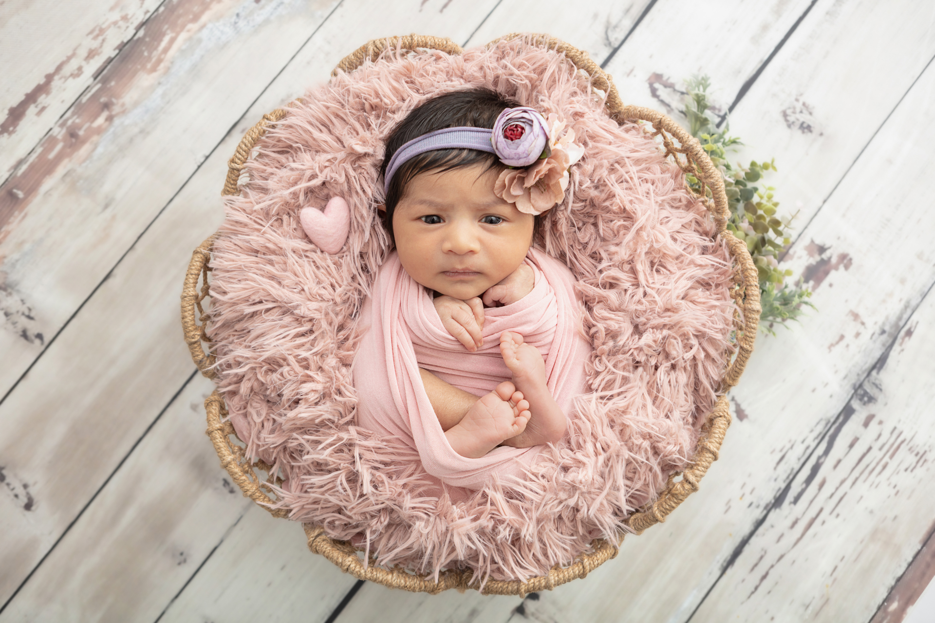 newborn baby girl with a lot of dark hair, wrapped in dusty pink with a felted pink heart