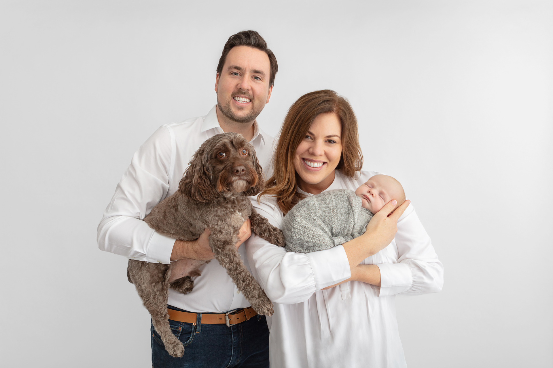 smiling new family of four; cockapoo, dad, mom, and baby boy; newborn family portrait with dog