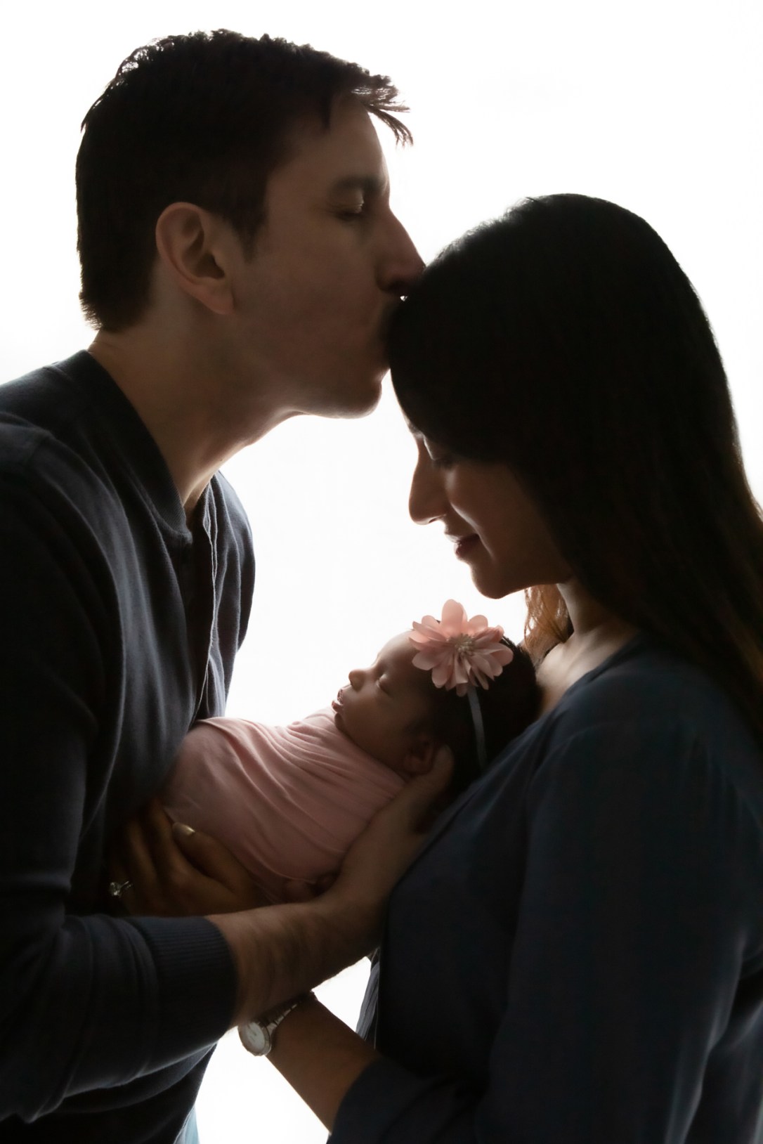 backlit silhouetted image of a new mother and new father holding their newborn baby girl in between them