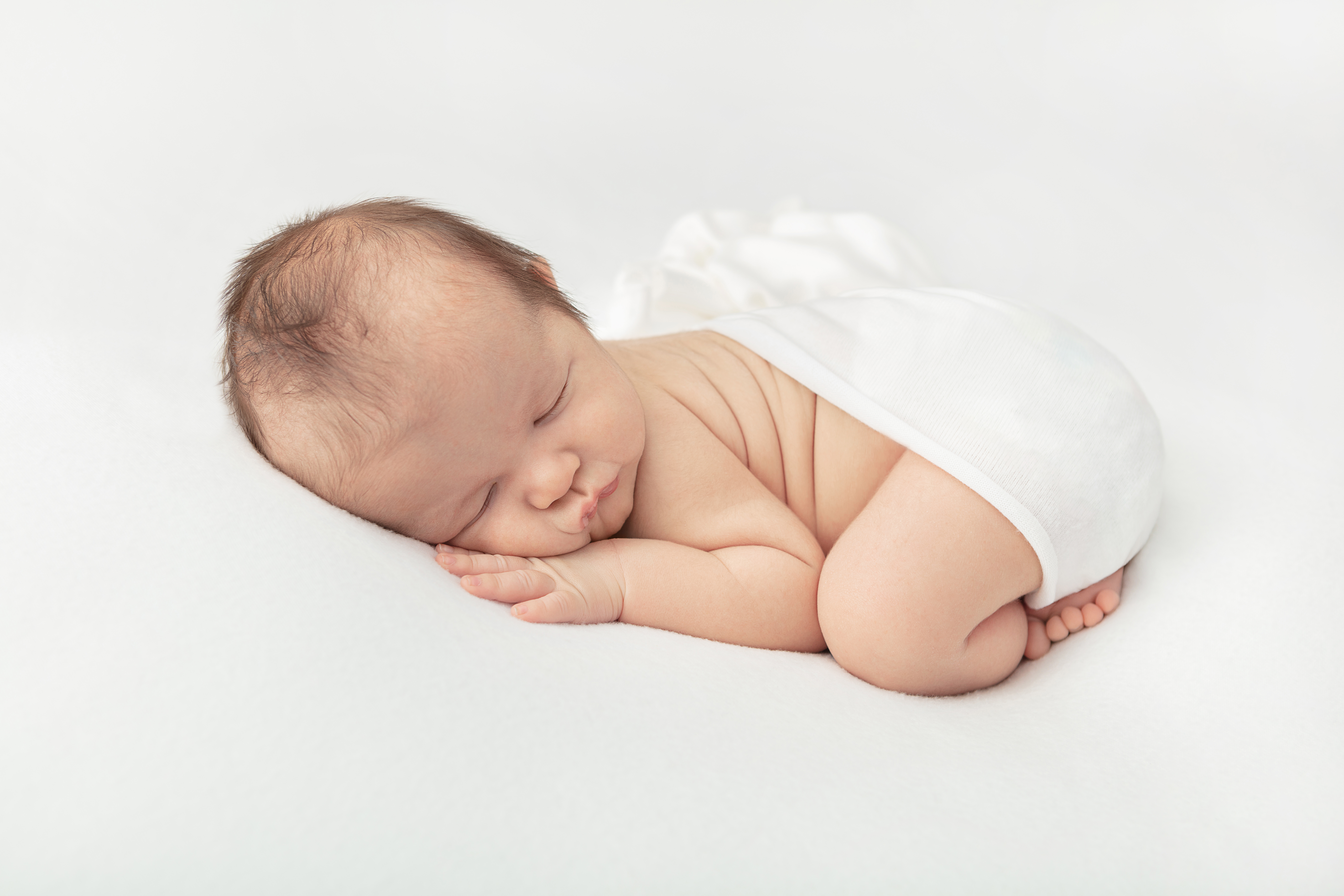 newborn baby boy asleep on a bed of white, swaddled in white