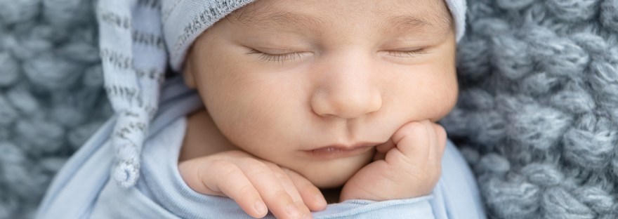 Newborn portrait session in the studio with baby boy wrapped in light blue laying on a soft knit light blue fabric and an adorable sleepy night cap hat in blue