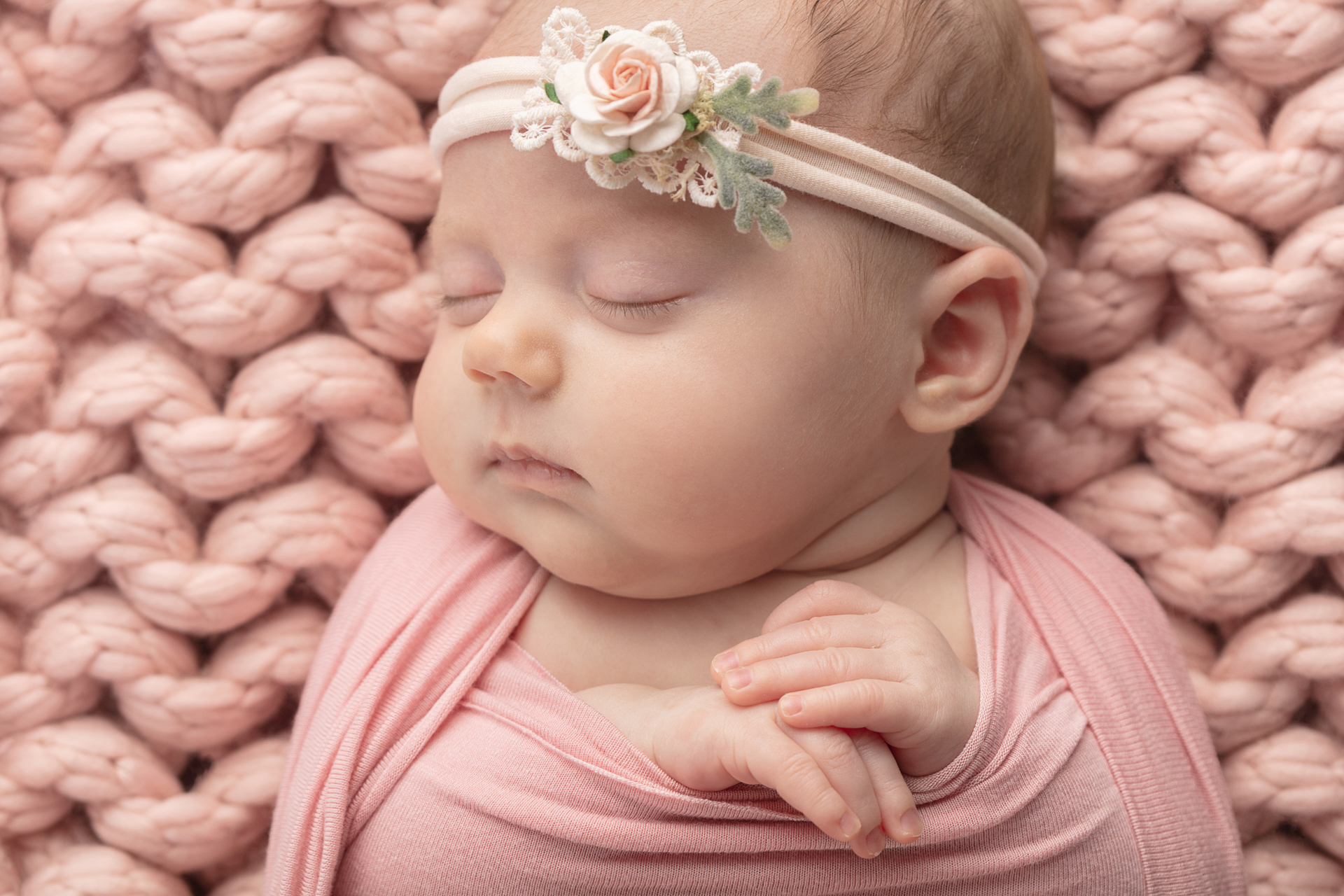 newborn girl swaddled in light pink with her folded hands peeking out from the swaddle