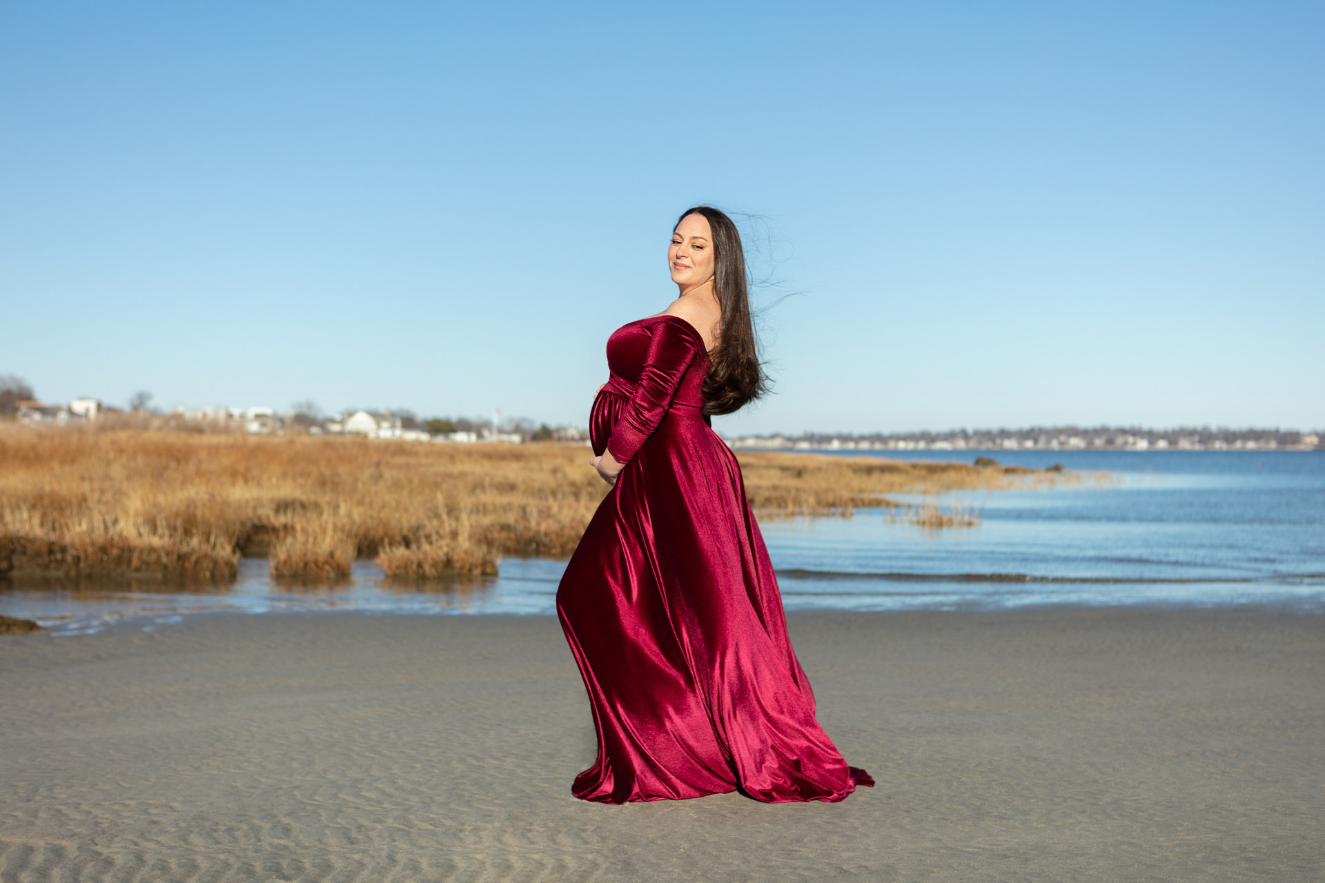 pregnant mama to be wearing a red velvet dress, standing on the beach at Tod's Point; Looking Up Photography