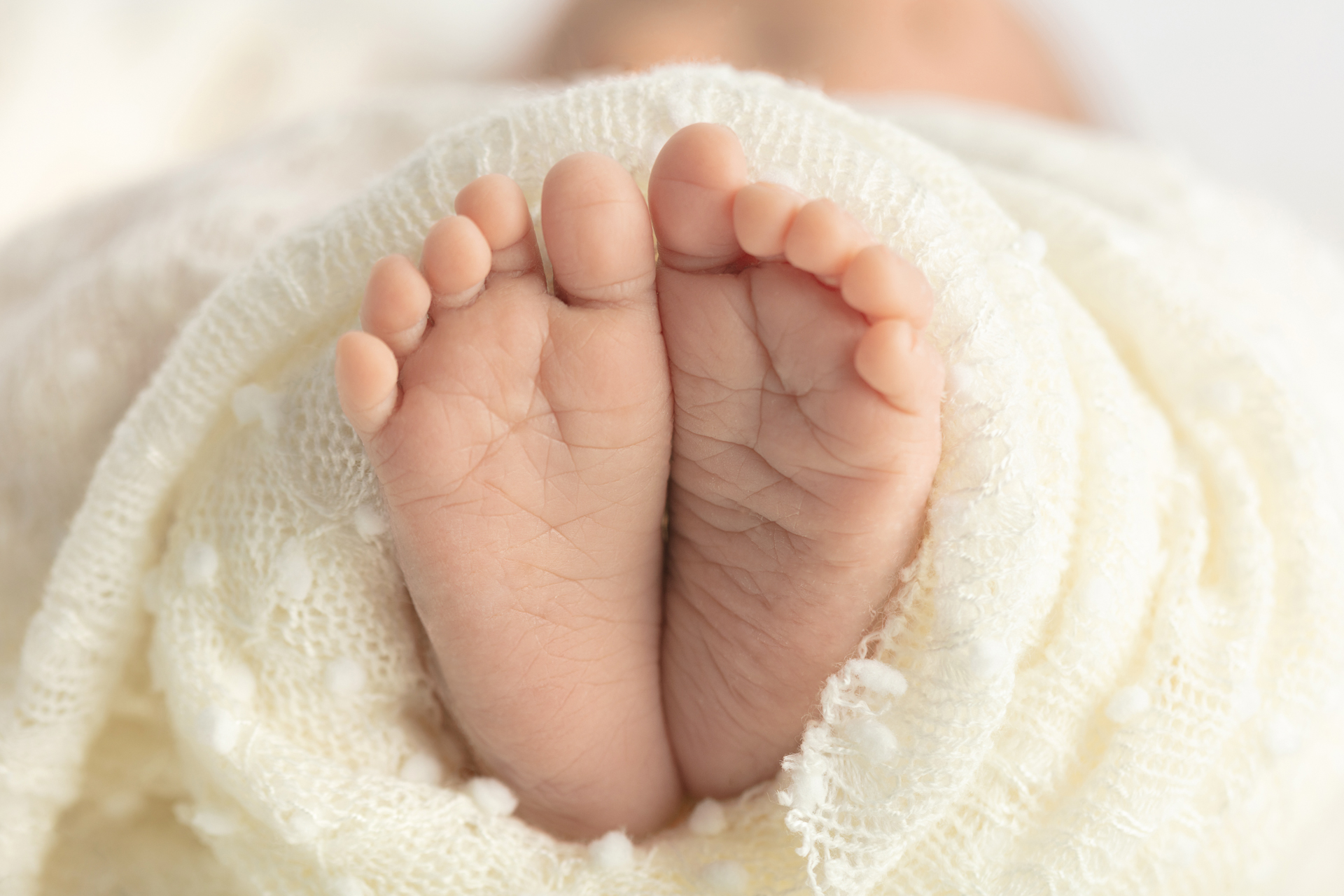 newborn feet and toes peeking from an ivory colored open knit blanket; Looking Up Photography