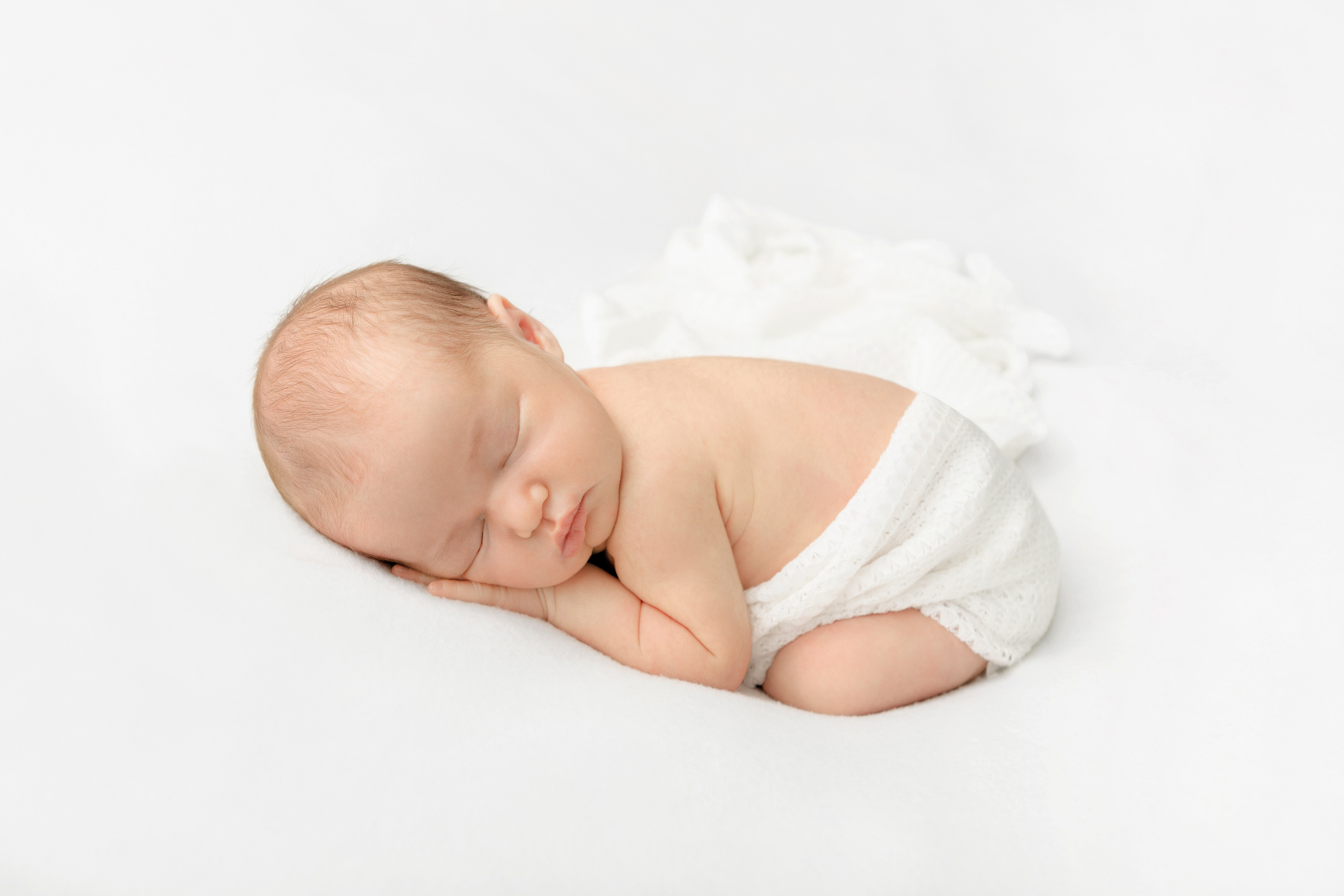 newborn baby girl sleeping on her hands, with her feet folded underneath her